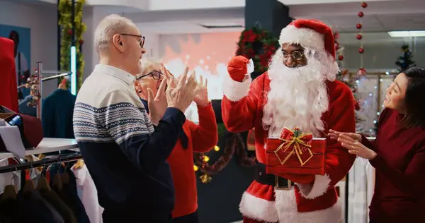 Sprzedawca Garniturze Świętego Mikołaja Świątecznym Zdobią Butiku Mody Trzymając Obecne — Zdjęcie stockowe