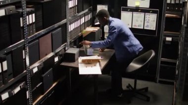 Özel dedektif elinde dizüstü bilgisayar çantasıyla ofisten çıkıyor. O gün için ayrılmadan önce, Afro-Amerikan polisi kişisel bilgisayarını kapatıp masasını düzenliyor. Hava görüntüsü.