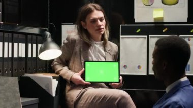 Siyahi polis izole edilmiş bir telif alanı görüntüsünü incelerken Kafkas özel dedektifi tableti yeşil ekranla tutuyor. Ofiste, kromakey model şablonlu dijital cihaz kullanan iki dedektif.