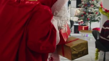 Noel Baba gibi giyinmiş bir müdürün festival süsleme ofisine bayram neşesi yayıp çalışanlarına hediyeler sunduğu yakın plan. Yönetici Noel hediyeleriyle şirket çalışanlarını heyecanlandırdı
