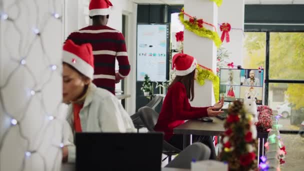 お祝いの装飾オフィスでクリスマスシーズン中にチームメイトとビデオコールのアジア人スタッフ 忙しいXmasオルネイトの職場でチームとのテレコンファレンスミーティングの従業員 — ストック動画