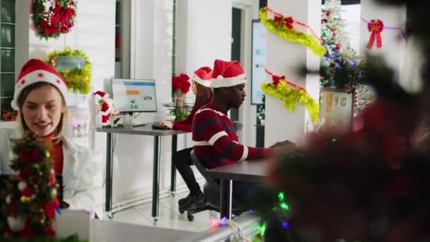 一个微笑的非洲商人在装饰过的办公室里为圣诞节工作的画像 冬季节日期间 与同事一起在不同工作场所的办公桌前解决员工问题 — 图库视频影像