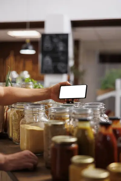Client in zero waste shop using mockup mobile phone to analyze pantry staples. Vegan customer thoroughly checking local supermarket food items are allergens free with isolated screen smartphone