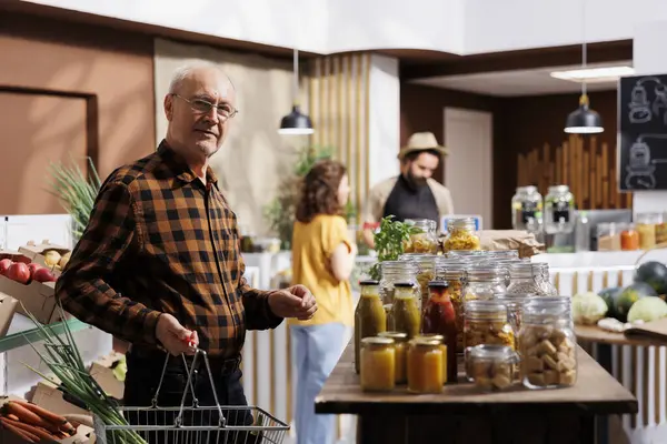 Portrait of elderly man looking for fresh vegetables in eco friendly zero waste store. Aged customer doing grocery shopping, buying organic natural food items in local neighborhood store