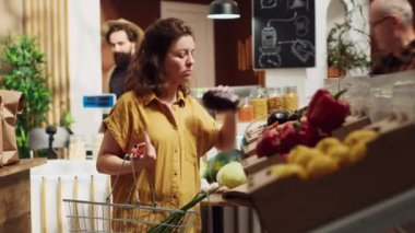 Çevre dostu sıfır atık süpermarketindeki vejetaryen kadın alışveriş sepetine etik kaynaklı organik sebzeler ekliyor. Mahalledeki dükkânda sürdürülebilir canlı müşteri tarım ürünleri topluyor.