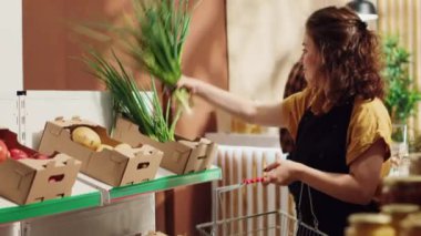 Sıfır atık süpermarketinde çalışan bir kadın rafları taze ürünlerle dolduruyor. Deponun rafları yakın zamanda yerel markete yeni toplanmış sebzeler geldi.