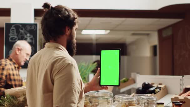 無駄なスーパーマーケットの単離されたスクリーン スマートフォンを使用して健康なレシピのための材料を点検する男 地元の食料品店のクライアントは 有機野菜の買い物中にモックアップ携帯電話を使用しています — ストック動画