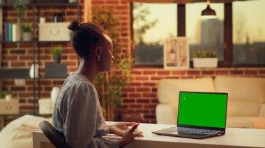 Kadın ekranda yeşil ekranda el sallıyor, görüntülü telefonda biriyle konuşuyor ve serbest meslek ediniyor. Boş maket ekranlı dizüstü bilgisayar kullanan kişi, gün batımında internet toplantısına katılın.