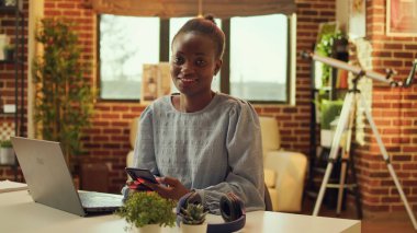 Günlük işleri ve ağ bağlantılarını çözmeden önce web sayfasında serbest çalışan ve sosyal medya uygulamalarını kontrol eden bir kadın. Afrika kökenli Amerikalı tele-işçi gün batımında masada oturuyor..