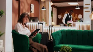Dinlenme odasında dinlenen otel misafiri, modern tablet kullanarak restoranlar ve ziyaret edilecek yerler buluyor. Tüm kapsayıcı tatil beldelerine seyahat eden yaşlı kişi odayı görmek ve keşfetmeye başlamak için bekliyor..