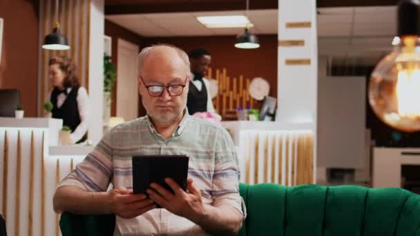 Starszy Mężczyzna Sprawdza Połączenie Tabletu Hotelu Relaksując Się Salonie Przed — Wideo stockowe