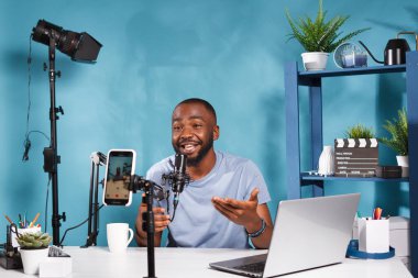 Blog yazarı akıllı telefonla video çekiyor ve internet kanalı aboneleriyle konuşuyor. Afrikalı Amerikalı vlogger konuşuyor, sosyal medyada canlı yayında tripodda cep telefonu kullanıyor.