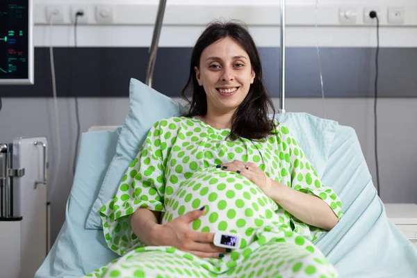 Portrait of smiling patient with pregnancy, waiting to receive medical examination from doctor to check healthcare. Woman expecting child and preparing to give birth in hospital ward
