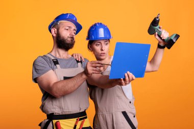 İnşaat işçileri kâğıtları analiz ediyor, ölçümleri not alıyor. Bilgi oluşturma veya yenileme ile ilgili dosyalara bakan inşaatçılar, elektrikli matkap ile mühendislik becerileri.