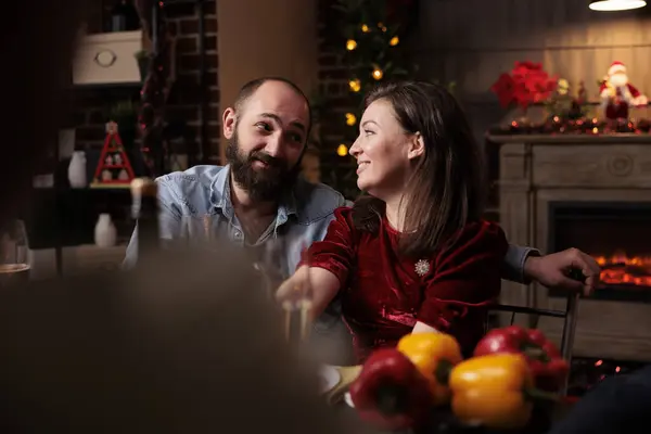 Sweet people meeting family at dinner on christmas eve, gathering around table with friends and relatives to eat traditional food and drink wine. Couple talking to persons during december event.