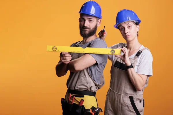 Construction workers holding screwdriver and water level in studio shot, using ruler or leveler to work on renovation. Team of building experts being confident with renovating tools.