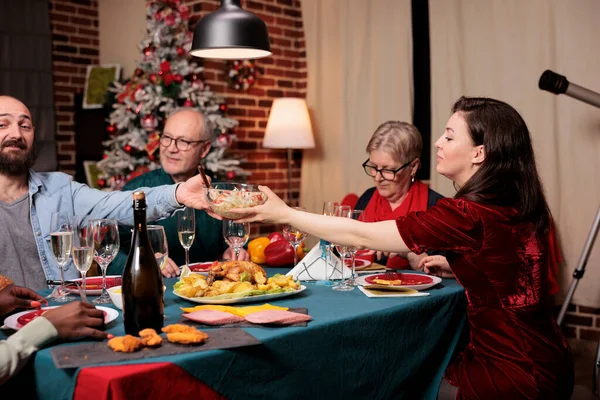 Family eating festive meal at dinner, celebrating Christmas eve together and passing food plates around the table. Cheerful people meeting during xmas celebration holiday, party feast.