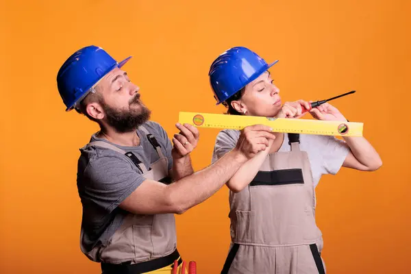 Contractors holding screwdriver and water level tool in studio shot, using ruler or leveler to work on renovation. Team of building experts being confident with renovating tools.