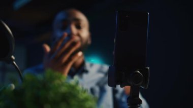 Çevrimiçi platformlar için video çekmek için loş ışıklı ev stüdyosunda çevrimiçi yıldız tarafından kullanılan akıllı telefonun aşırı yakın çekimi. Kaydetmek için bulanık arkaplanda nüfuz eden kişi tarafından kullanılan telefon