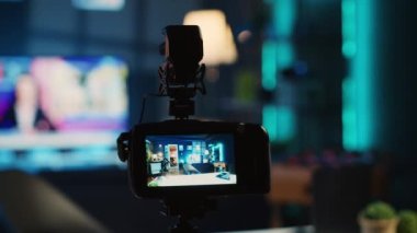 Çevrimiçi platformlar için video çekmek için loş ışıklandırılmış ev stüdyosunda çevrimiçi yıldız tarafından kullanılan üç ayaklı kameranın aşırı yakın çekim görüntüsü. Etkilenen kişi tarafından çekimleri yakalamak için kullanılan boş odada kayıt cihazı