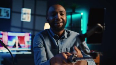 BIPOC içerik yaratıcısı, selfie çubuğu akıllı telefonu kullanıyor, hayranları için rahat dairesini gösteren bir video hazırlıyor. Cep telefonu kamerası kullanarak çevrimiçi yayın sırasında izleyicilerle konuşan medya yıldızı