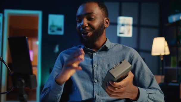 新しく発売されたポータブルVマウントバッテリーのビデオレビューを撮影するアフリカ系アメリカ人のコンテンツクリエイターは それを解除し 視聴者に提示します 視聴者のための充電デバイスのボックスを記録するメディアスター — ストック動画