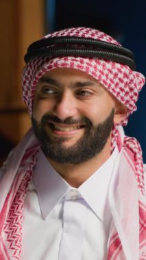 Gülümseyen Arap serbest çalışanın dikey video portresi, bütün gün bilgisayarında yazdıktan sonra mola veriyor, kapatıyor. Geleneksel giyimli, başörtüsü takan Ortadoğulu bir adam,