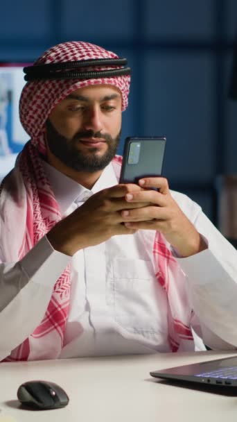 Вертикальное Видео Арабский Мужчина Дома Гостиной Печатает Сообщения Смартфоне Мусульманин — стоковое видео
