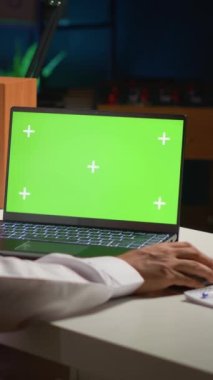 Dikey videolu Arap adam evden çalışırken model dizüstü bilgisayarda kayıyor. Daire ofisindeki izole ekran cihazına arka plan gürültüsü olarak TV ile e-posta yazan serbest çalışan kişi