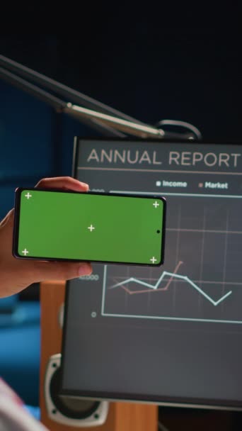 コンピュータのビジネス年次報告グラフを見ながら 景観モードで緑色のスマートフォンを保持する垂直ビデオリモートワーカー 中東フリーランサーとモックアップ携帯 — ストック動画