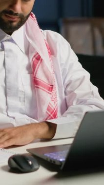 Ev ofisinin bilgisayarında çalışan dikey video Arap girişimci internete göz atıyor ve deftere yazıyor. Müslüman adam telgraf çekerken kalem, not defteri ve dijital aygıt kullanıyor
