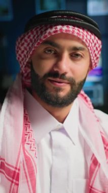 Geleneksel kıyafetler giymiş neşeli Müslüman içerik yaratıcısının dikey video görüntüsü kendini filme çekiyor. Gülümseyen Arap adam tobe ve başörtüsüyle kameraya doğru el sallıyor, çevrimiçi video blogu yapıyor.