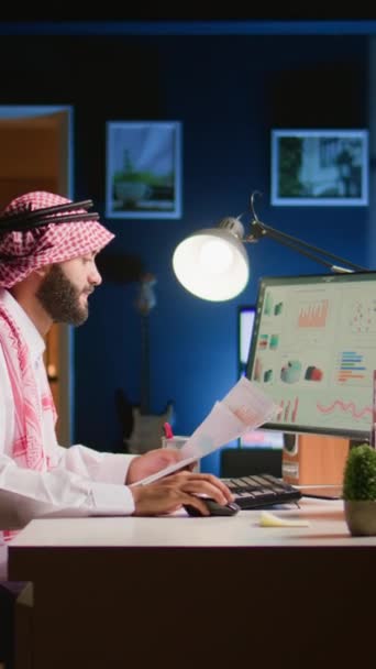 在光线昏暗的公寓办公室远程工作的同时 垂直视频穆斯林远程工作者横切分析统计数据集与文书工作 努力工作的阿拉伯员工优化关键绩效 — 图库视频影像