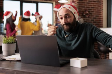 Noel Baba şapkalı aşırı stresli beyaz adam Noel sezonunda dizüstü bilgisayarla çalışıyor. Yılbaşı tatilinde bilgisayarın son başvuru tarihine kadar çalışmaktan yorulmuş.