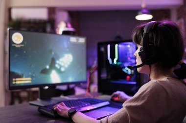 Profesyonel oyuncu son teknoloji oyun sistemini kullanarak online çok oyunculu turnuvaya katılıyor, canlı yayında hayranları cezbediyor. RGB ışıklarıyla aydınlatılmış oturma odasında video oyunları oynayan bir kadın.