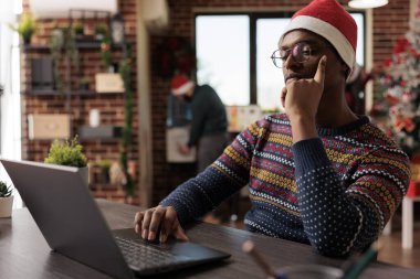 Noel Baba şapkalı Afro-Amerikan bir şirket çalışanı Noel tatilinde dizüstü bilgisayarda çalışıyor. Festivalin dekore edilmiş işyerindeki proje raporunu yönetirken işçiler düşünüyor