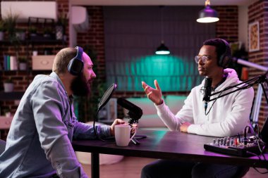 Podcast sunucusu ve konuk sunucusu birbirleriyle tartışıyor ve ev stüdyoda canlı yayında tartışmalar yapıyorlar. Neon ışıklı adamlar oturma odasında internet izleyicileri için konuşuyorlar.