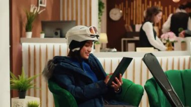 Lobide tablet üzerinde gezen bir kadın, dış giyim ve kaskla kayak yapmak için donanımlı. Kayak merkezindeki Asyalı gezgin kayak takımlarıyla kış sporlarının tadını çıkarıyor. El kamerasıyla..