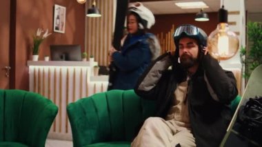 İnsanlar salonda kayak malzemeleriyle oturup yamaçlardan kaymaya hazırlanıyorlar. Aktif erkek ve kadın teçhizatlarını kontrol edip dağ evinde kış sporları yapmaya gidiyorlar..