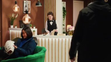 Turist, Alp disiplini kayak merkezine vardıktan sonra personelden yamaç talebinde bulunuyor, resepsiyonist lobideki kış sporları meraklısını selamlıyor. Kayak ve koruyucu giysi taşıyan genç bir adam kayıyor..