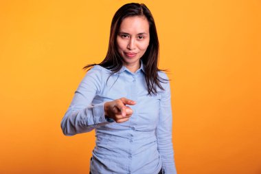 Başarılı Asyalı kadın seni işaret ederek stüdyoda sarı arka planda poz veriyor. Gamsız gülümseyen genç yetişkin işaret parmağıyla reklam ürünü gösteriyor. Reklam kavramı