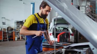 Araba servisindeki tamirci, motoru değiştirdikten sonra cıvataları sıkmak için iş yerindeki banktan tork anahtarı seçiyor. Otomobil tamircisi müşteri otomobilini tamir etmek için profesyonel araçlar kullanıyor
