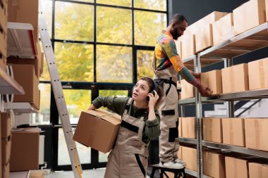 Depo ekibi müşterilerin siparişleriyle dolu raflara bakıyor, kulaklıklarda müzik dinlerken karton kutu taşıyor. Çok ırklı çalışanlar depoda teslimat için ürün paketleri hazırlıyorlar