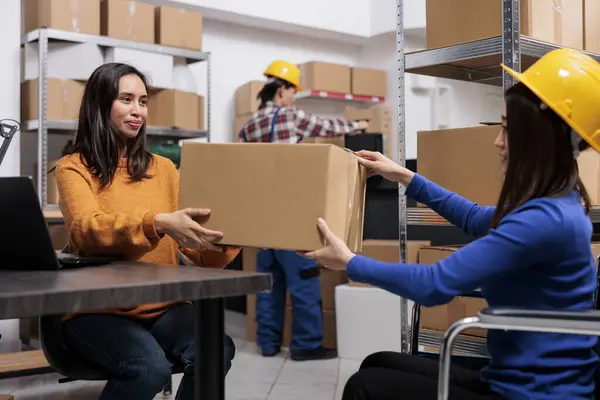 Asian warehouse worker with disability giving package to colleague. Storehouse logistics manager and product picker inspecting order quality and preparing for sending in storage room