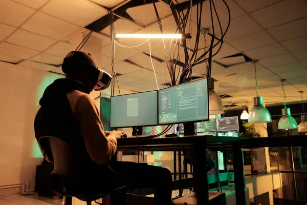 Male hacker working to hack server with vr 3d headset, planning cyberattack with virtual reality at night. Young adult causng computer malware, using interactive glasses, cyberterrorism.