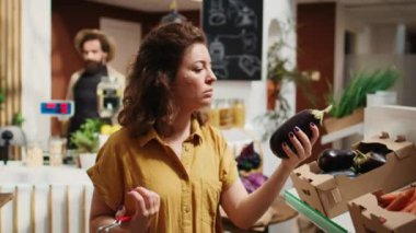 Sıfır atık süpermarket müşterisinin organik sebze bulmak için koridorlarda dolaşırken görüntüsü. Mahalle müşterisi sağlıklı yiyecek alışverişi yapıyor.