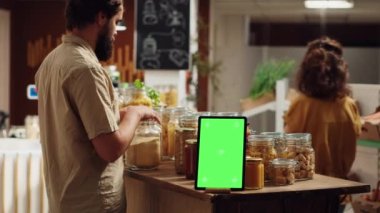 Sıfır atık süpermarketinde ticari tabela olarak kullanılan krom anahtar tabletinin yanındaki müşteri dükkanları. Gıda mağazasında yeşil ekran cihazına tanıtım reklamı ve kirletici olmayan paketler