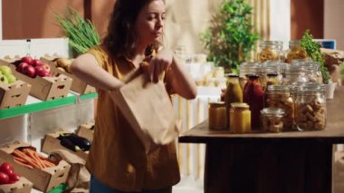 Sıfır atık süpermarketinde sağlıklı kiler zımbası alırken çürütülebilir kese kağıdı kullanan bir kadın. Tek kullanımlık plastik poliçesi olmayan yerel bir dükkanın müşterisi