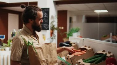 Çevre dostu dükkandaki müşterisi, çevre dostu kese kağıdına etik kaynaklı taze sebzeler ekliyor. Mahalledeki markette organik yiyecek arayan bir adam.