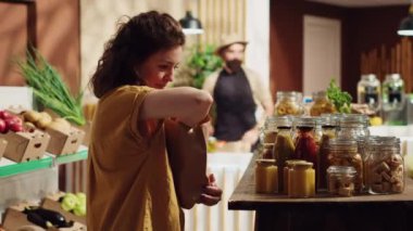 Sıfır atık süpermarketinde organik klozet zımbası alırken çürütülebilir kağıt poşet kullanan mutlu bir kadın. Tek kullanımlık plastik poliçesi olmayan mahallenin gülümseyen müşterisi.